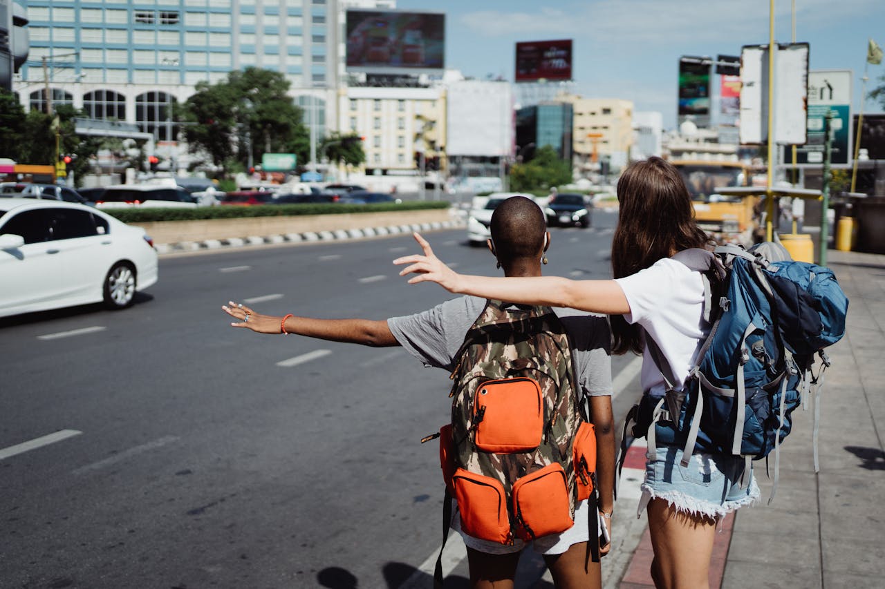 Two travelers with backpacks raising their arms at a busy city intersection.