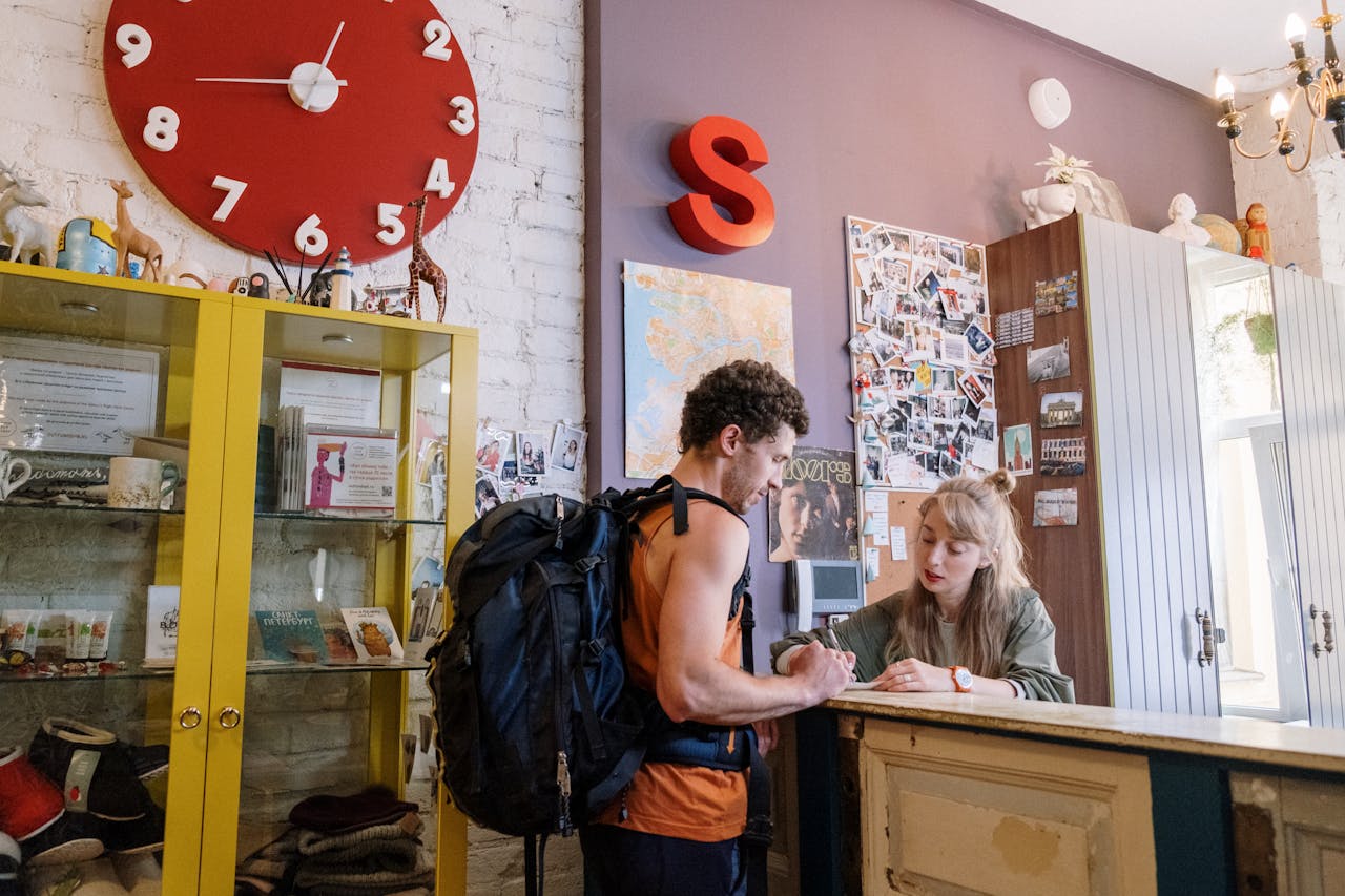 who-we-are A backpacker at a hostel front desk getting assistance from a receptionist.
